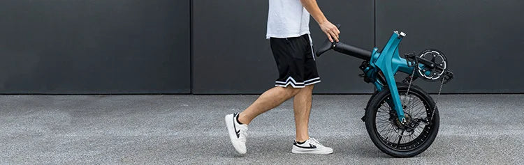 Un uomo esce spingendo una bicicletta elettrica pieghevole Fiido X ripiegata