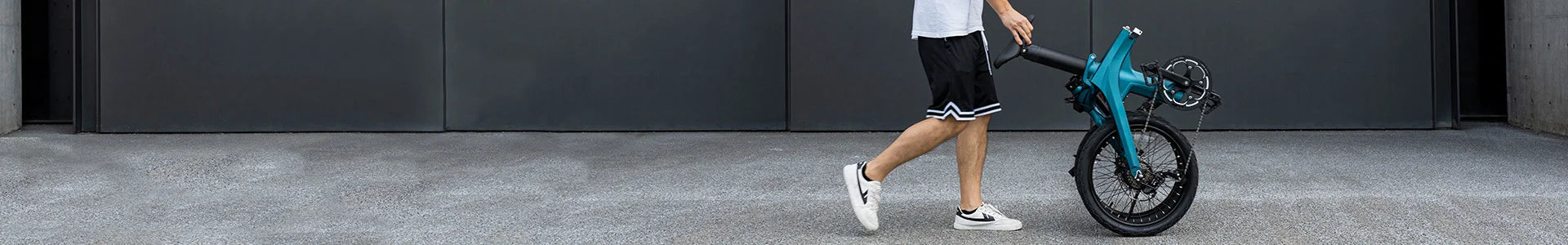 Un uomo esce spingendo una bicicletta elettrica pieghevole Fiido X ripiegata