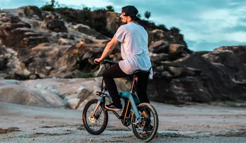 Un ciclista sul Fiido D11 che esplora un terreno costiero roccioso al tramonto.