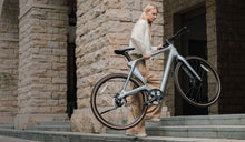 Una donna solleva senza sforzo una bici elettrica leggera Fiido Air su per le scale.
