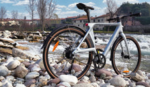 E-bike ultraleggera in fibra di carbonio Fiido Air esposta su una riva rocciosa accanto all’acqua corrente.