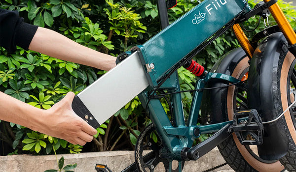 Un uomo sta rimuovendo la batteria esterna di una bicicletta elettrica Fiido M1 PRO.