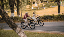 Due ciclisti in sella a e-bike da trekking Fiido Nomads Pro su una strada cittadina