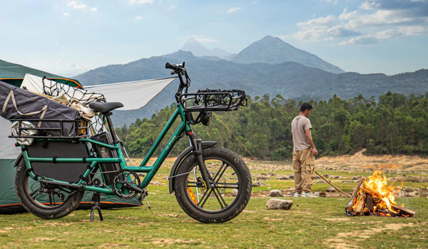 Bici elettrica cargo Fiido T2 carica di attrezzatura da campeggio in un campeggio di montagna, accanto a una tenda e a un falò